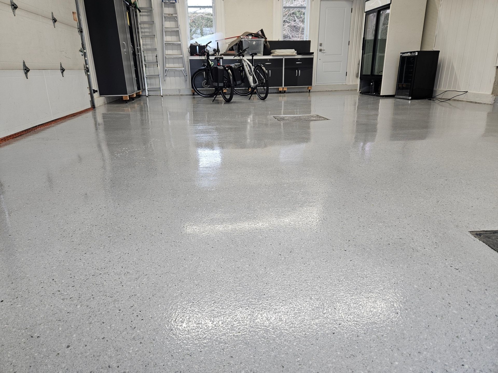 Glossy gray epoxy garage floor with scattered flecks, reflecting light.
