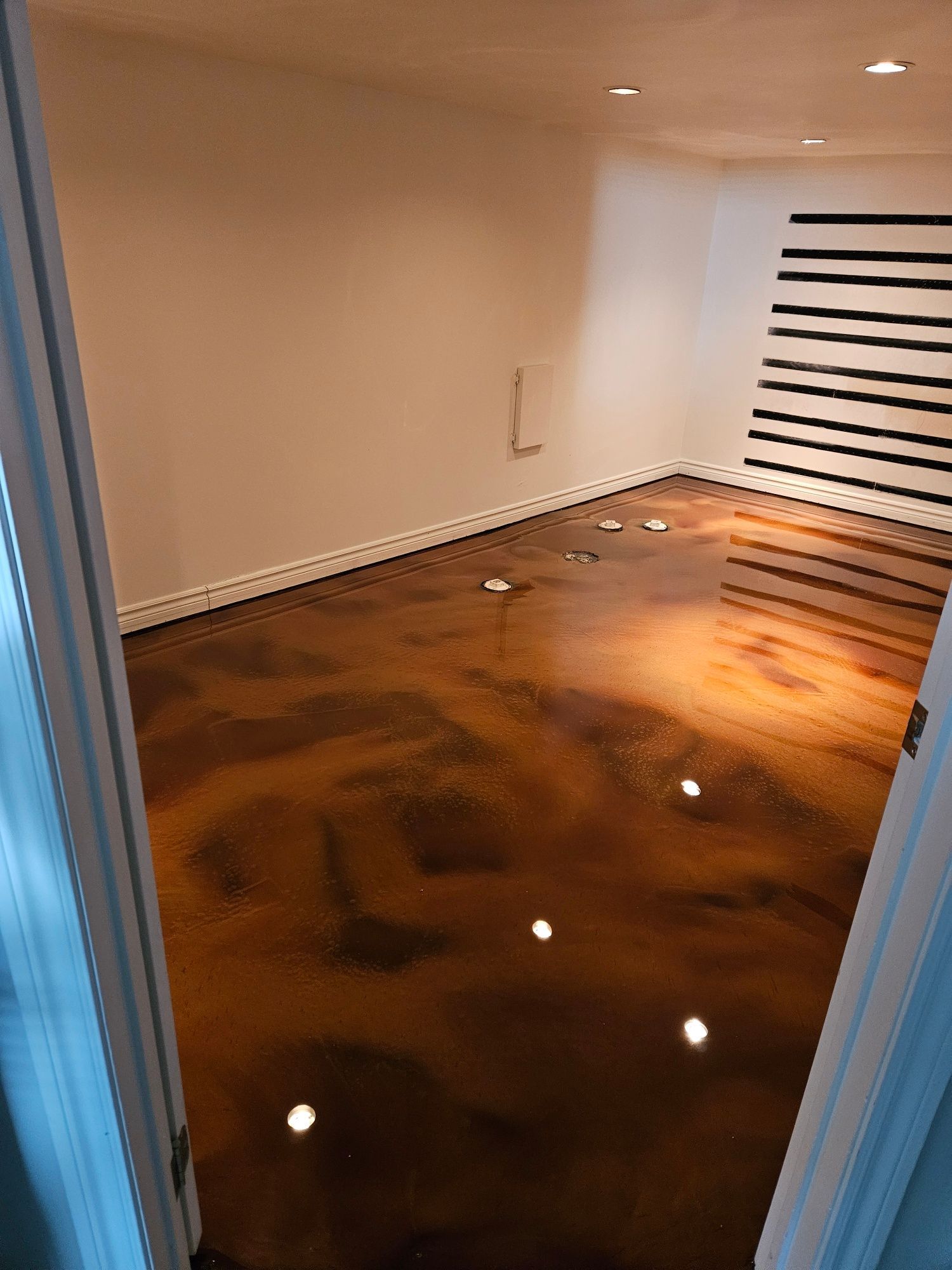 Room with glossy, brown floor and white walls. Black and white striped artwork.