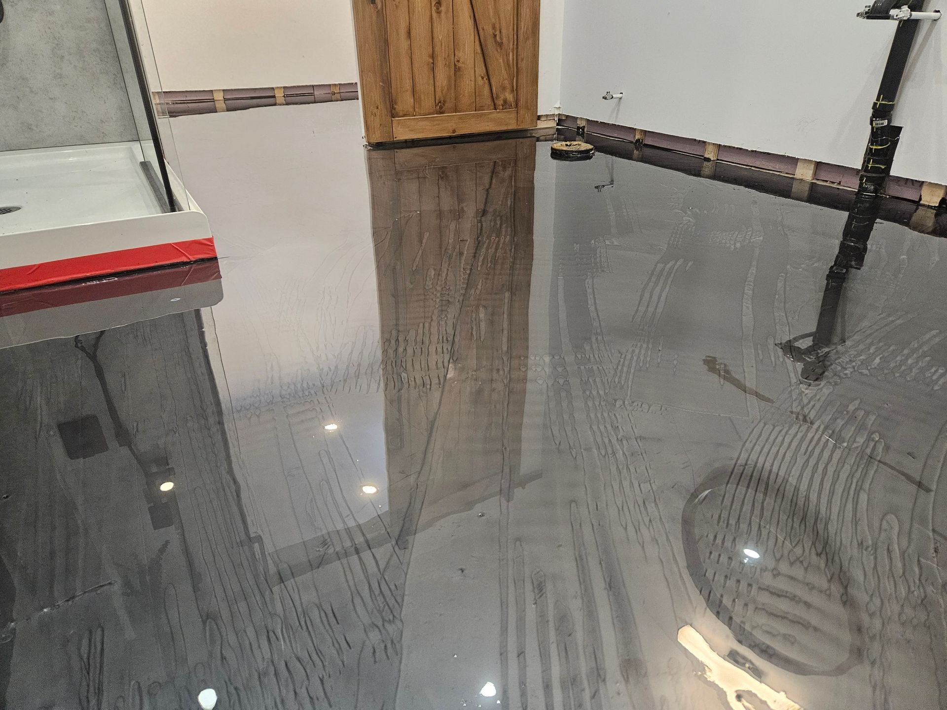 Dark, glossy epoxy floor reflecting a wooden door and a metal frame; setting is indoors.