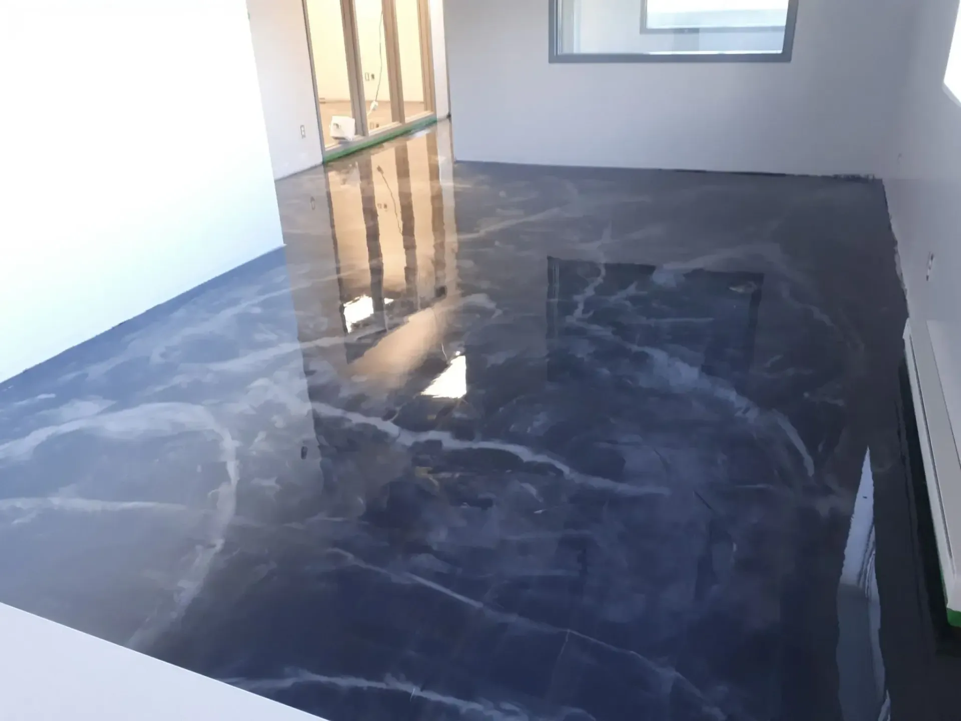 Shiny, dark gray and white marble-effect epoxy flooring in a room with white walls and a window.