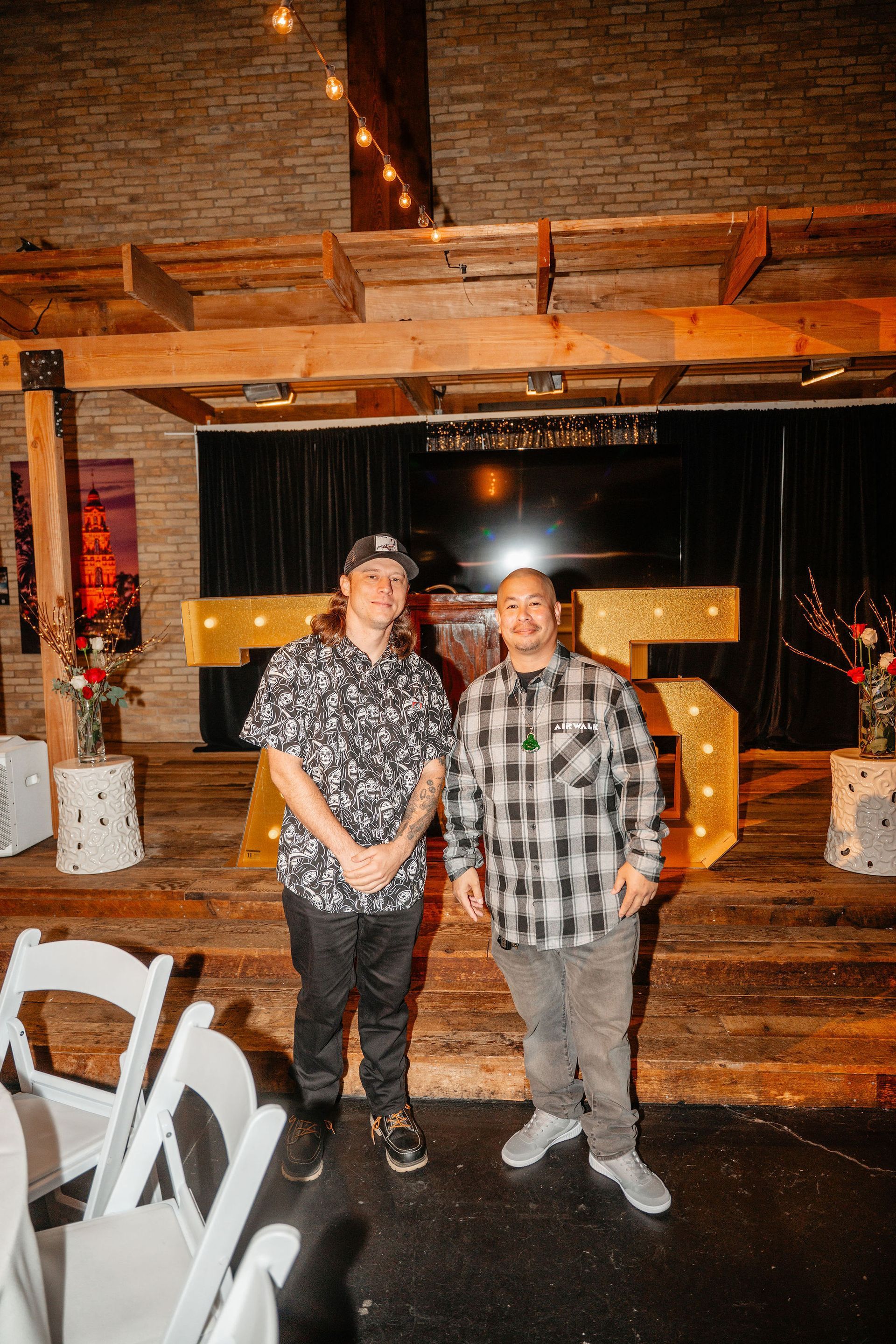Two men stand in front of a lit 