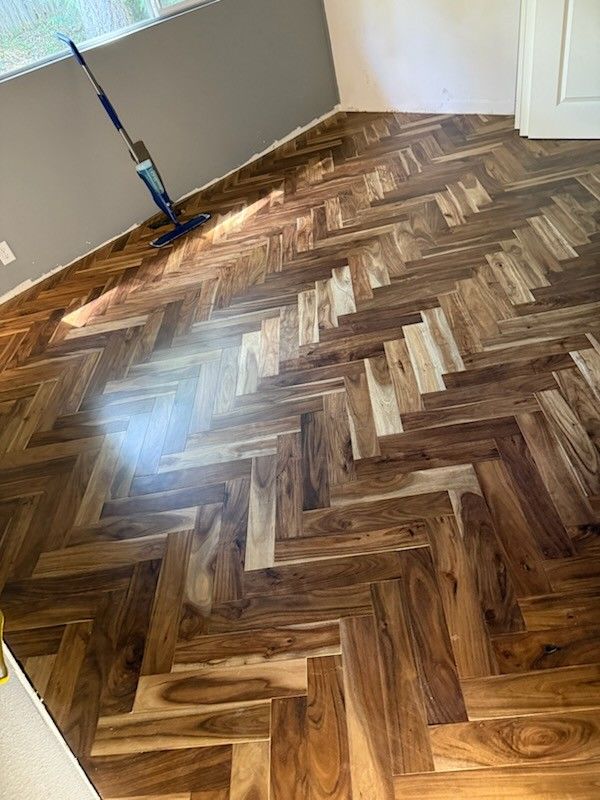 Close-up of a dark wood floor installed in a chevron or herringbone pattern with a blue mop resting on it.