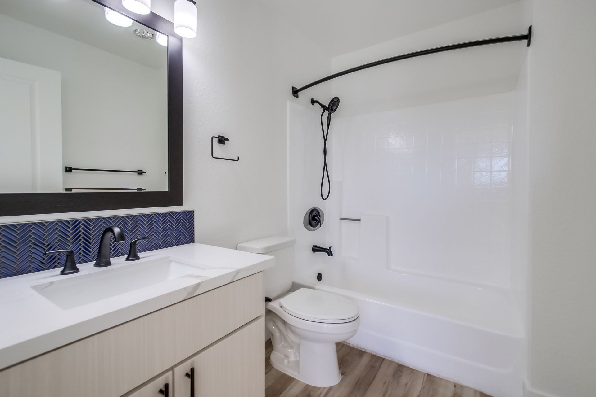 Bathroom with white walls, a bathtub, a vanity with blue tile, and black fixtures.