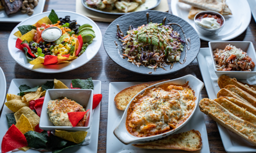 Various colorful dishes on a table, including salad, baked pasta, and appetizers.