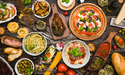 Italian food spread on a wooden table, featuring pasta, pizza, vegetables, and sauces.
