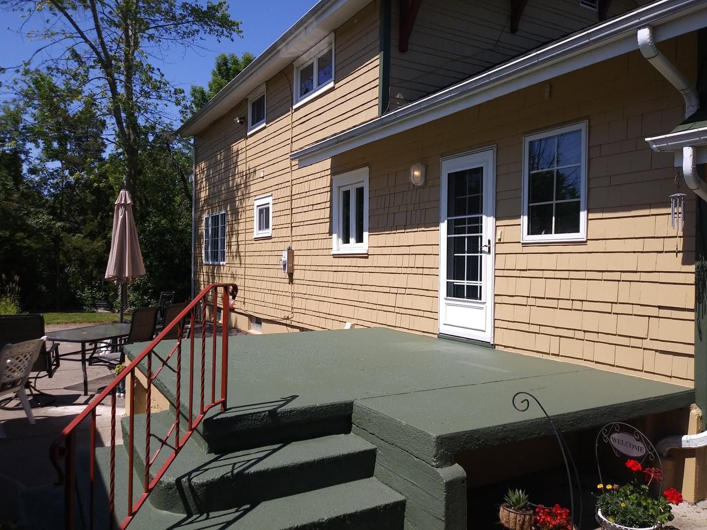 Back deck with green steps, red railing, and tan house siding beside patio furniture and umbrella