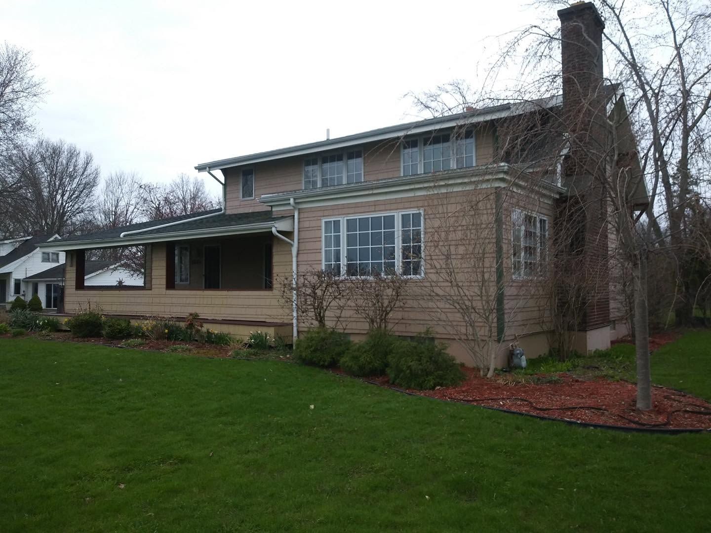 Brick house with a front porch, large windows, and a green lawn on an overcast day