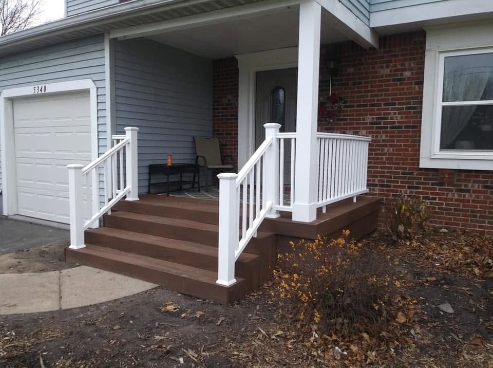 Front porch with brown steps, white railings, and a gray garage beside a brick and siding house.