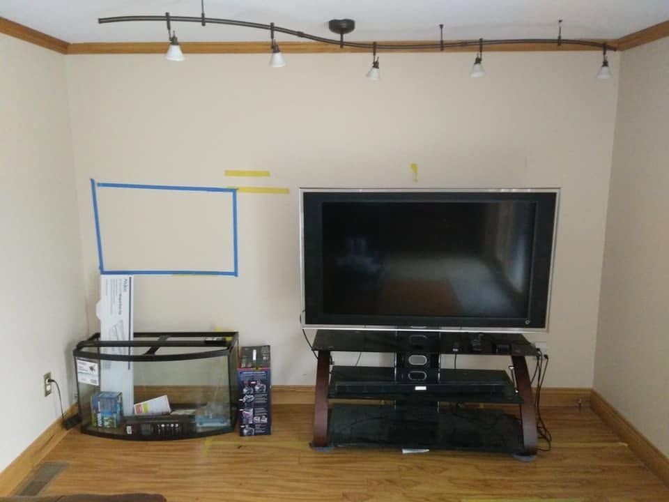 Living room with a wall-mounted TV, glass tank stand, and blue tape marking on the wall