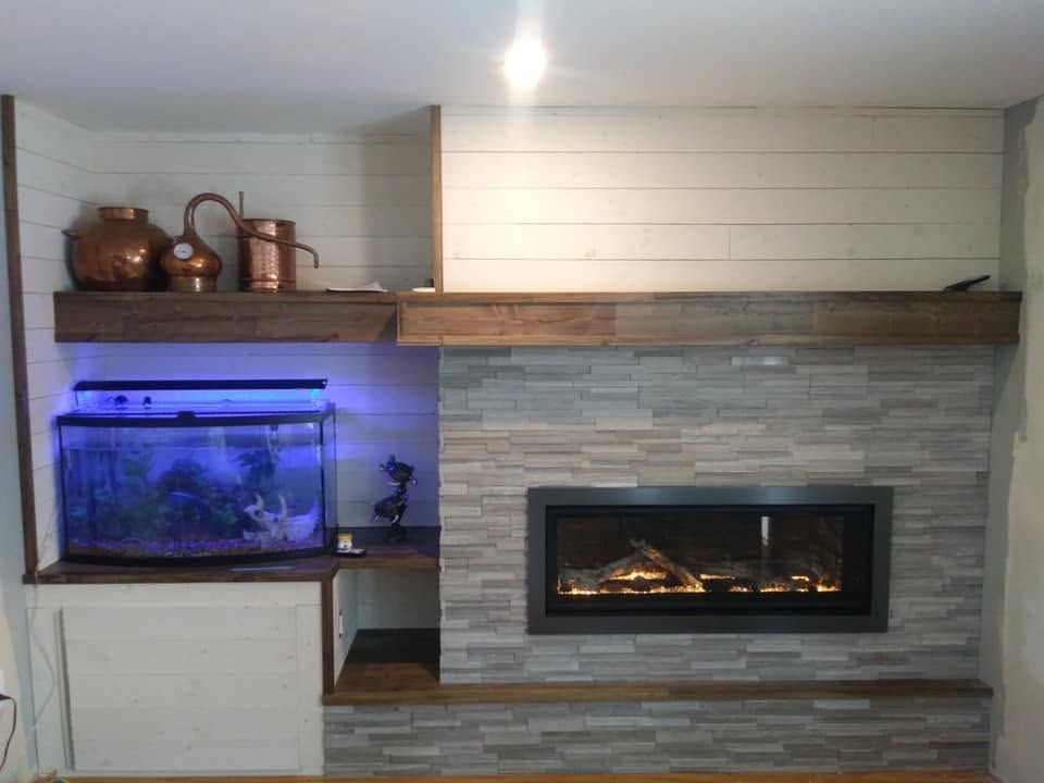 Modern living room with a stone fireplace, mounted fire, and blue-lit aquarium on the left.