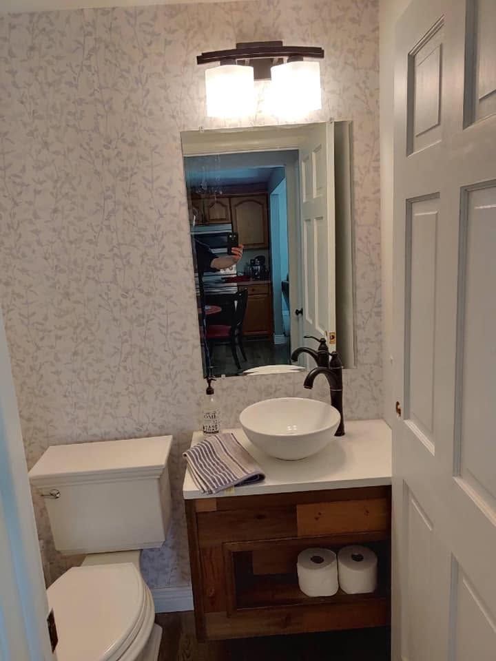 Small bathroom with a pedestal sink, mirror, toilet, and warm light above a wooden vanity.