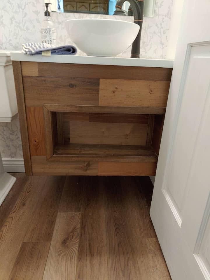 Wood bathroom vanity with white vessel sink and open shelf, seen from a doorway