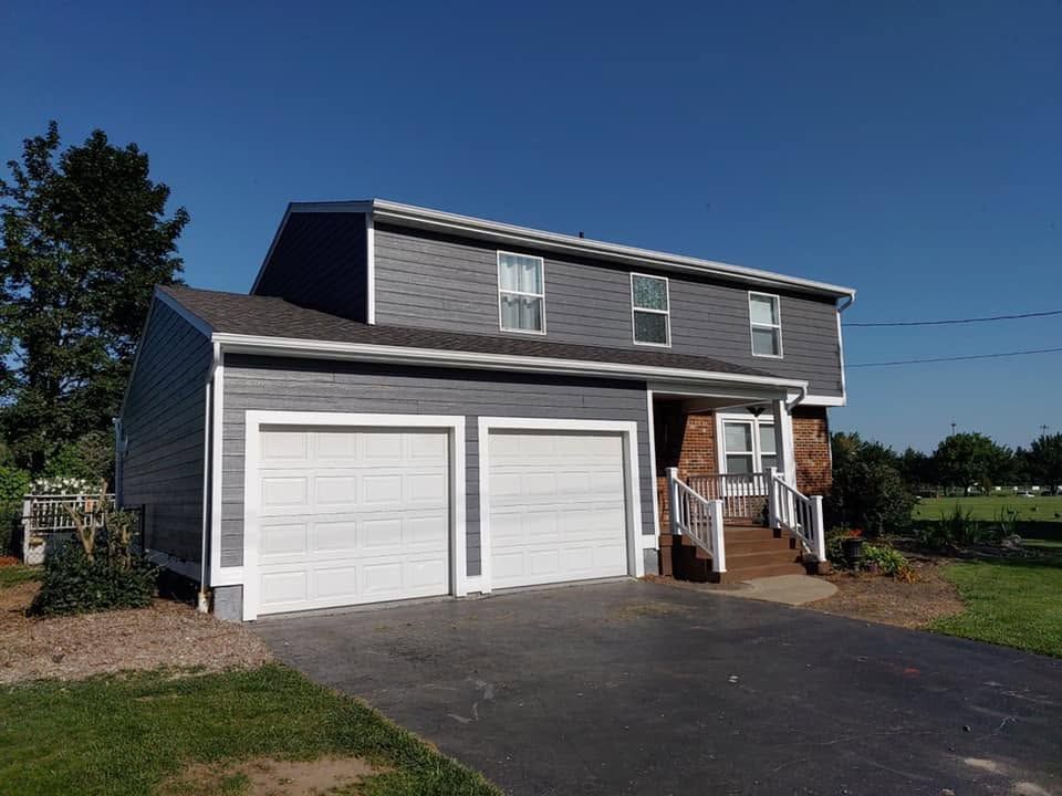 Two-story gray house with double garage doors and a driveway under a clear blue sky
