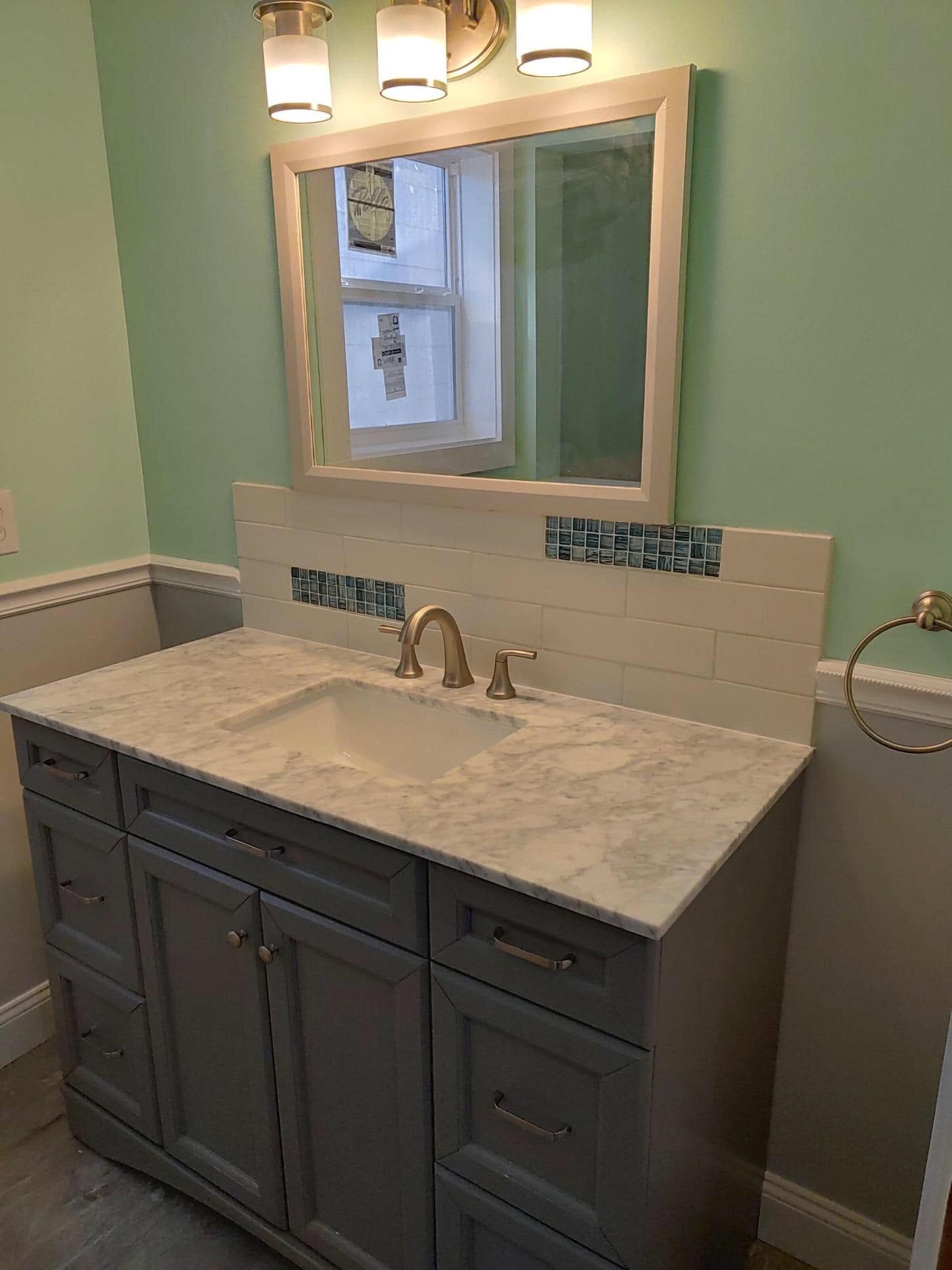 Bathroom vanity with dark gray cabinets, marble countertop, and framed mirror under wall lights