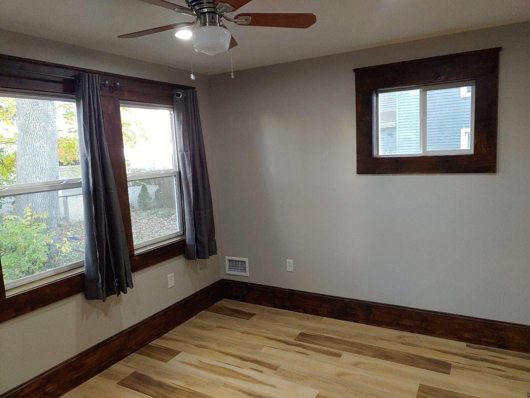Empty bedroom with wood floors, large windows, dark trim, and a ceiling fan