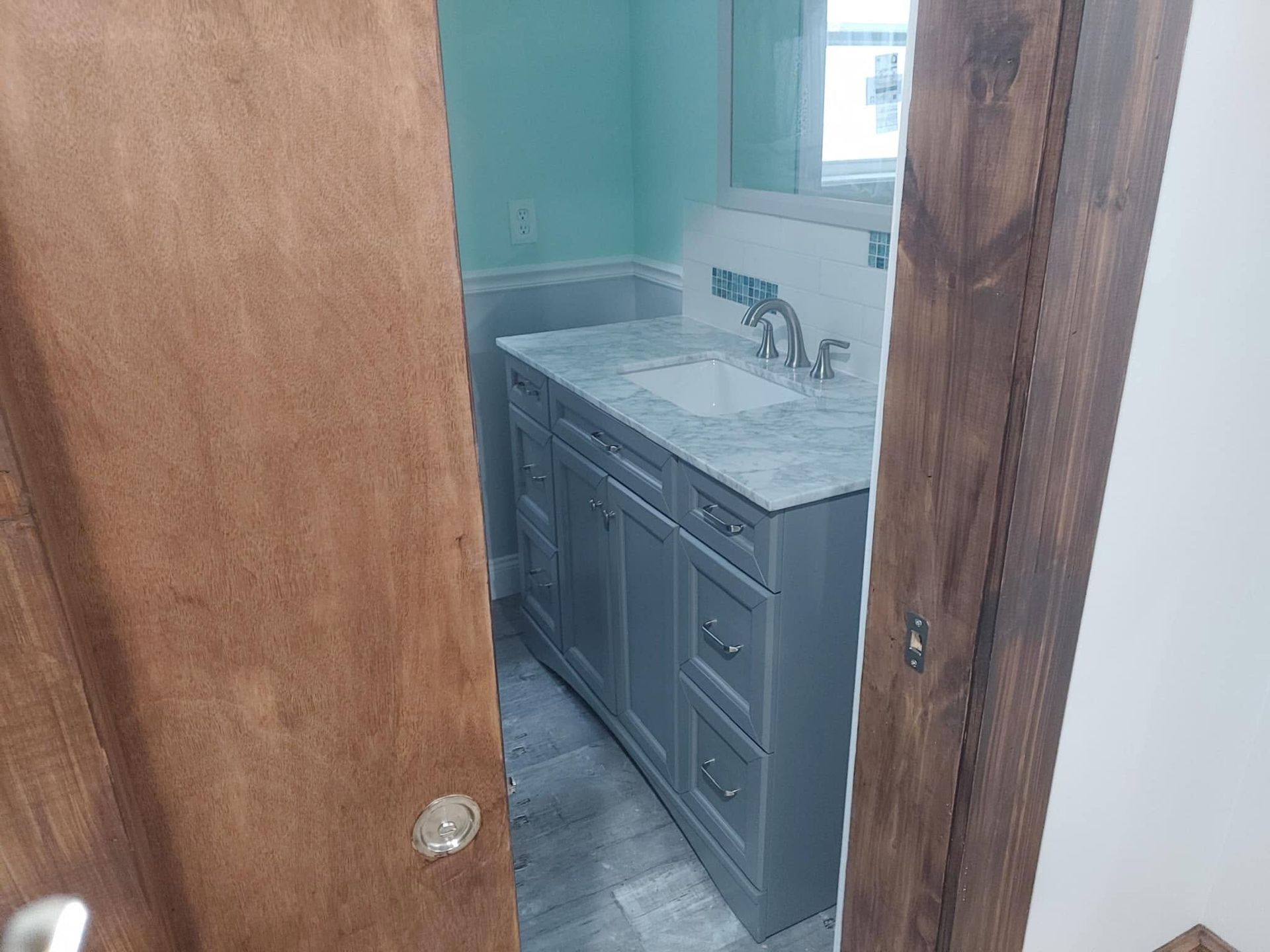 Partially open door revealing a bathroom vanity with gray cabinets and a white countertop sink