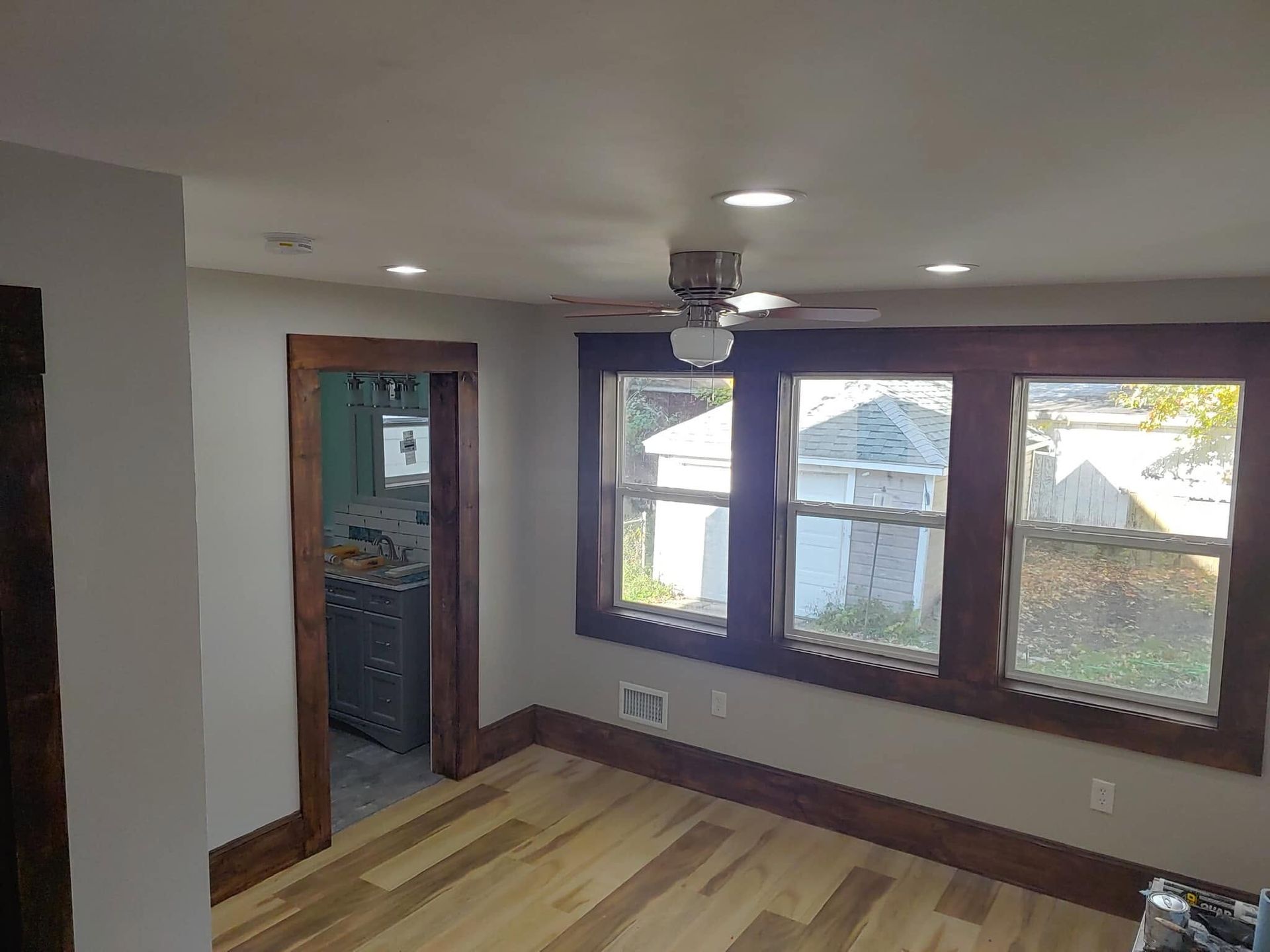 Empty room with wood floors, recessed lights, and large windows overlooking neighboring houses