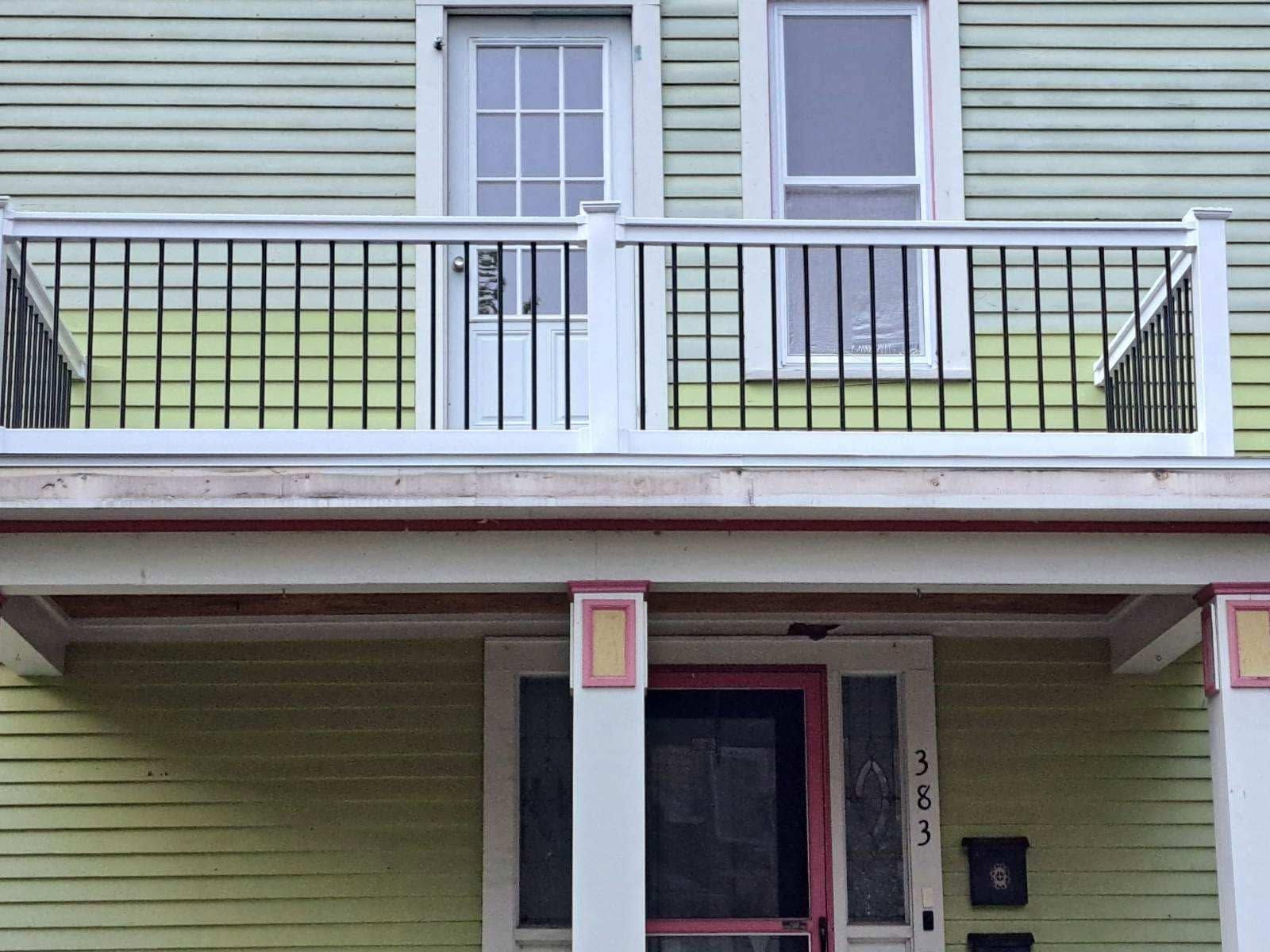 White balcony on a light green house with railing, windows, and a front door below