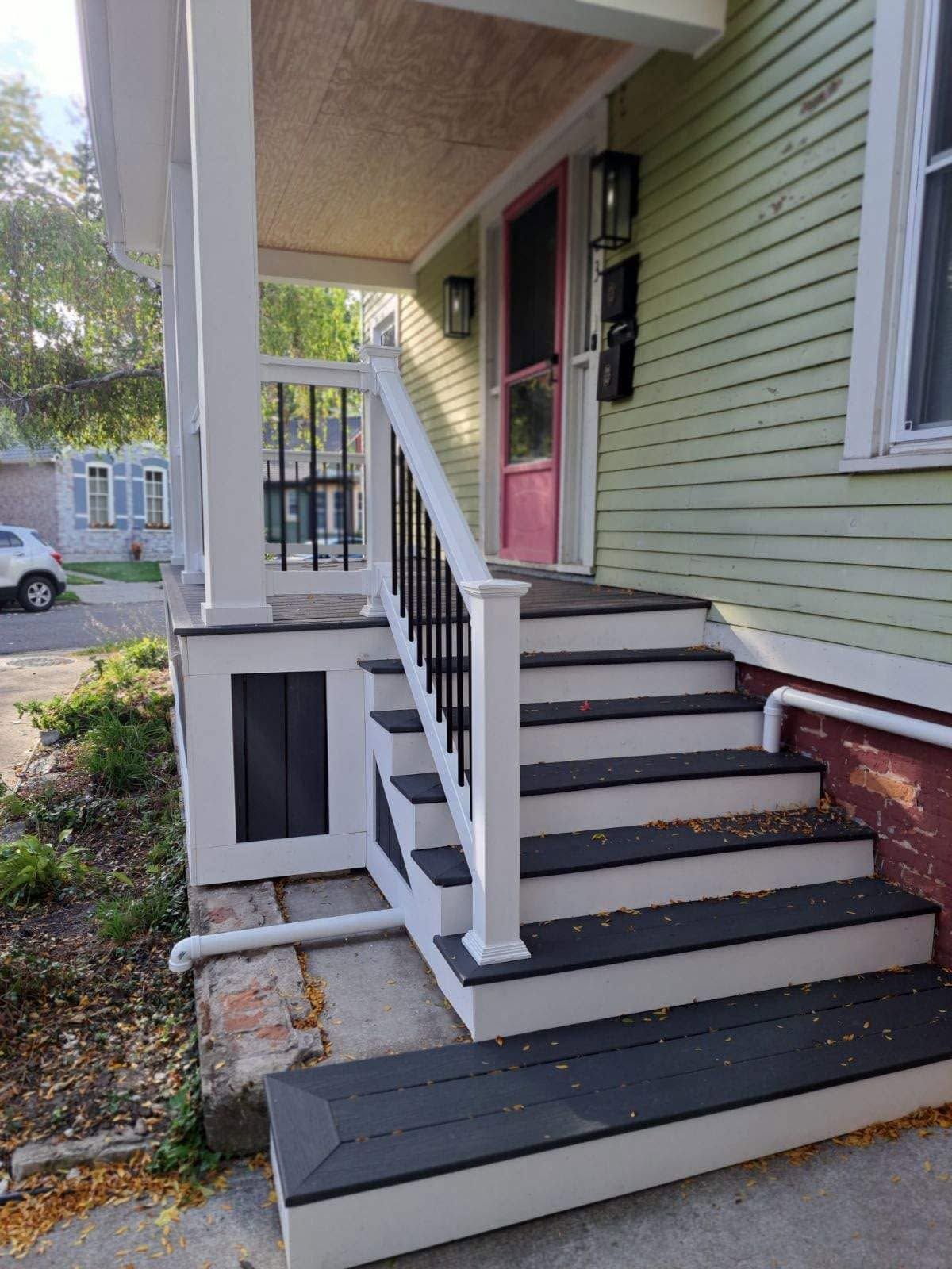 Front porch stairs with gray steps, white railings, and a dark wood landing on a green house