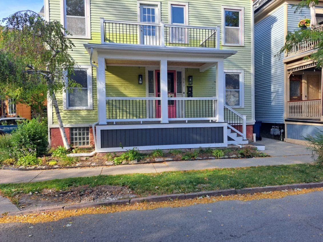 Front porch of a yellow house with white trim and a gray ramp beside the sidewalk.