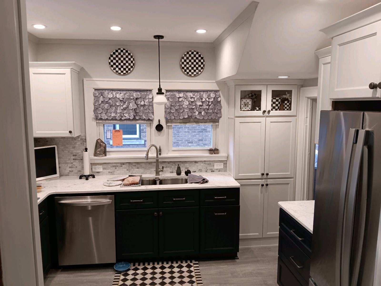 Modern kitchen with dark cabinets, stainless steel appliances, white countertops, and a window over the sink.