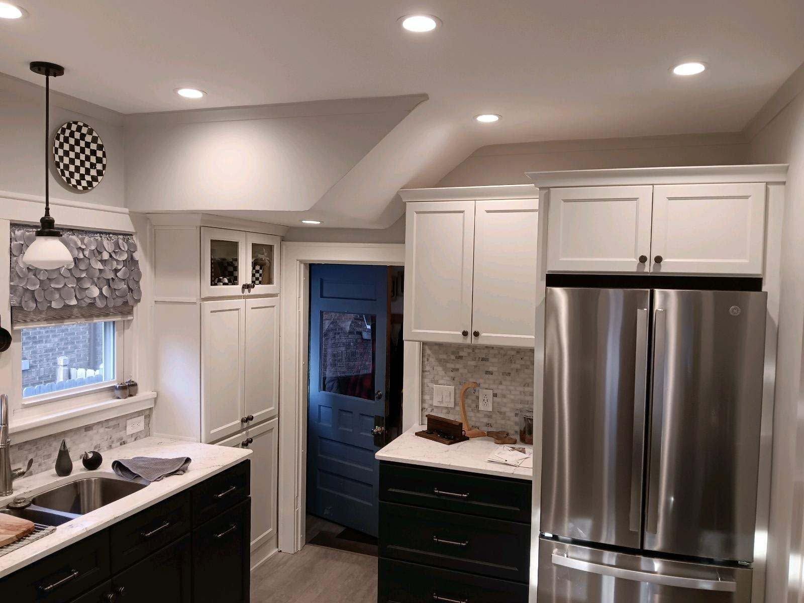 Bright kitchen with white cabinets, stainless fridge, black counters, and recessed ceiling lights