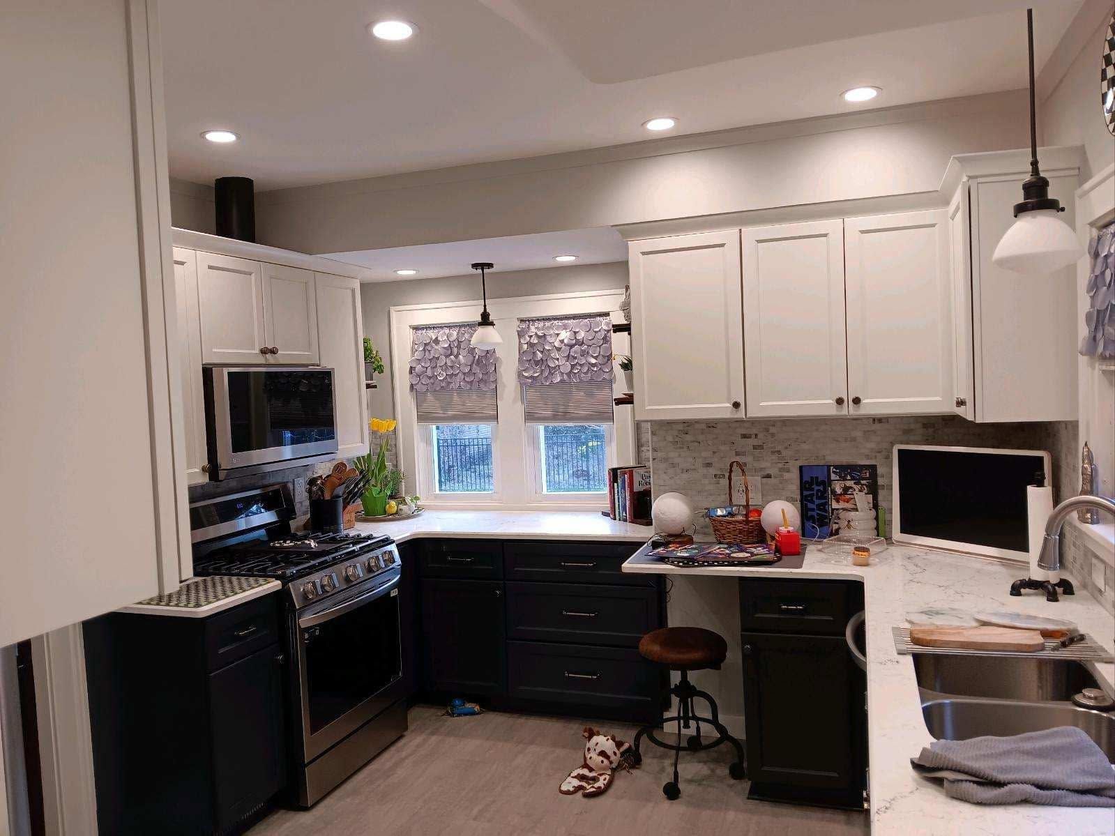 Bright modern kitchen with white cabinets, black appliances, and a sink under a window with patterned blinds