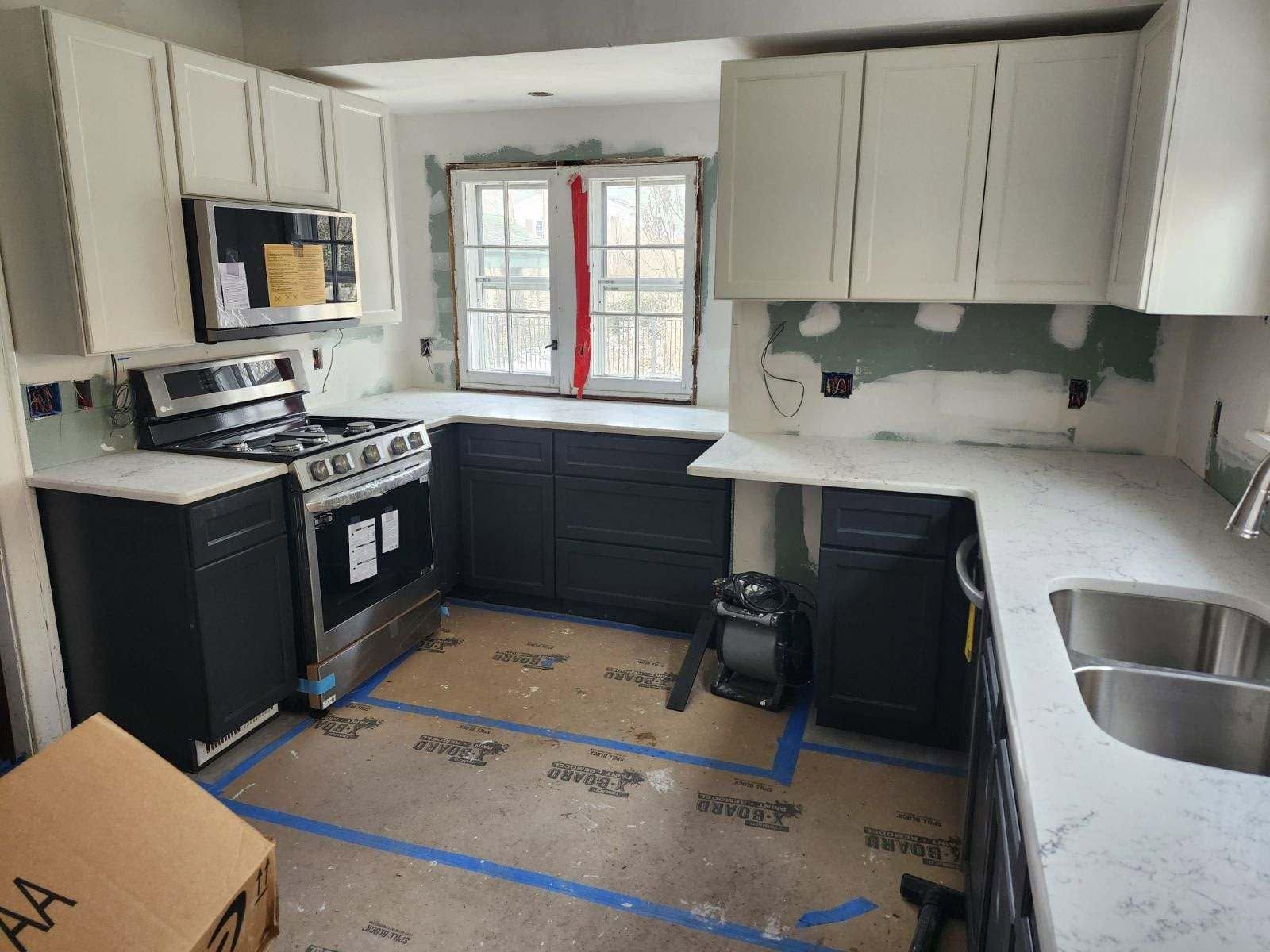 Renovated kitchen with black-and-white cabinets, stove, sink, and windowed back wall