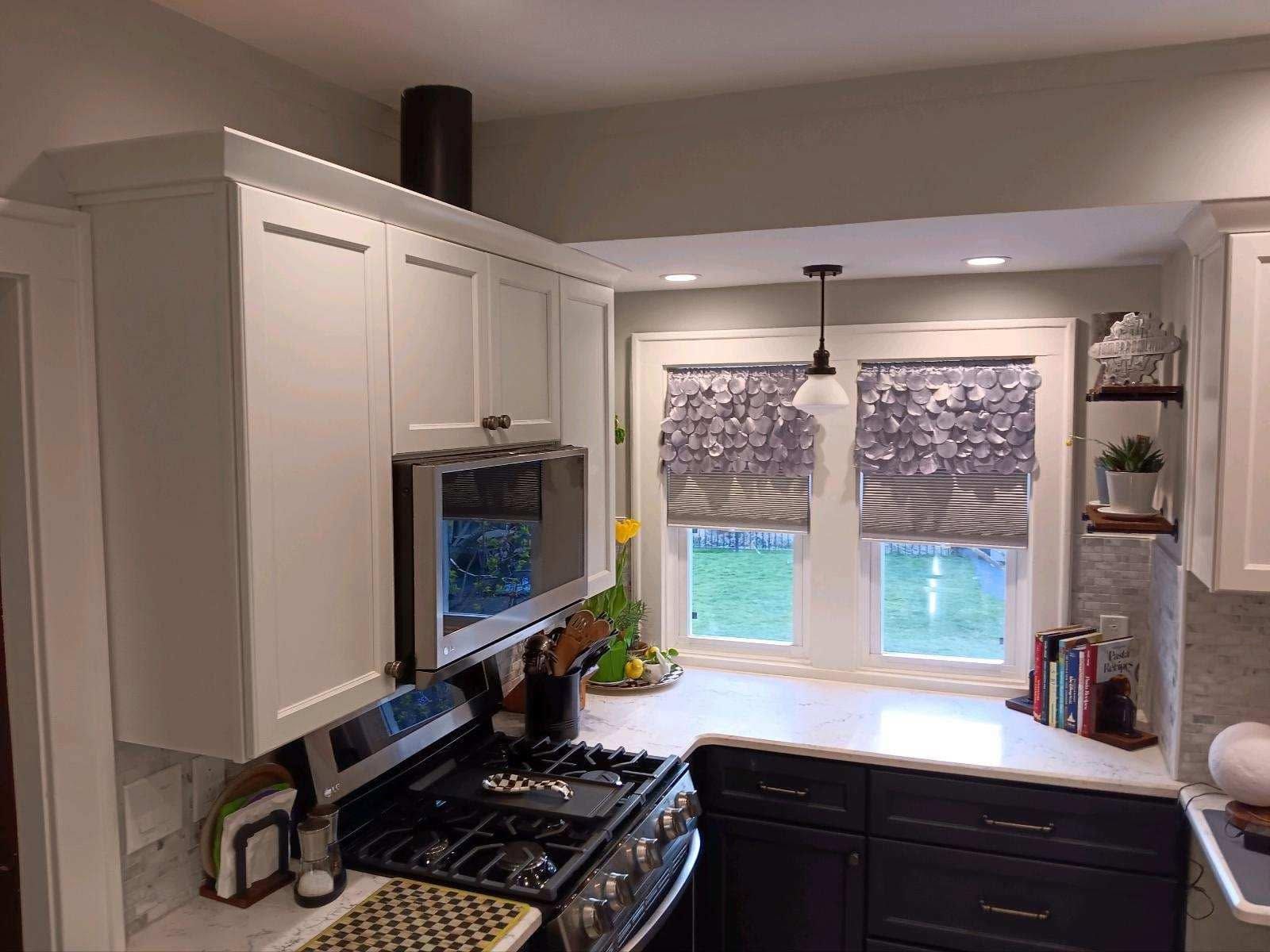 Bright kitchen with white cabinets, black stove, dark sink, and window over the counter.