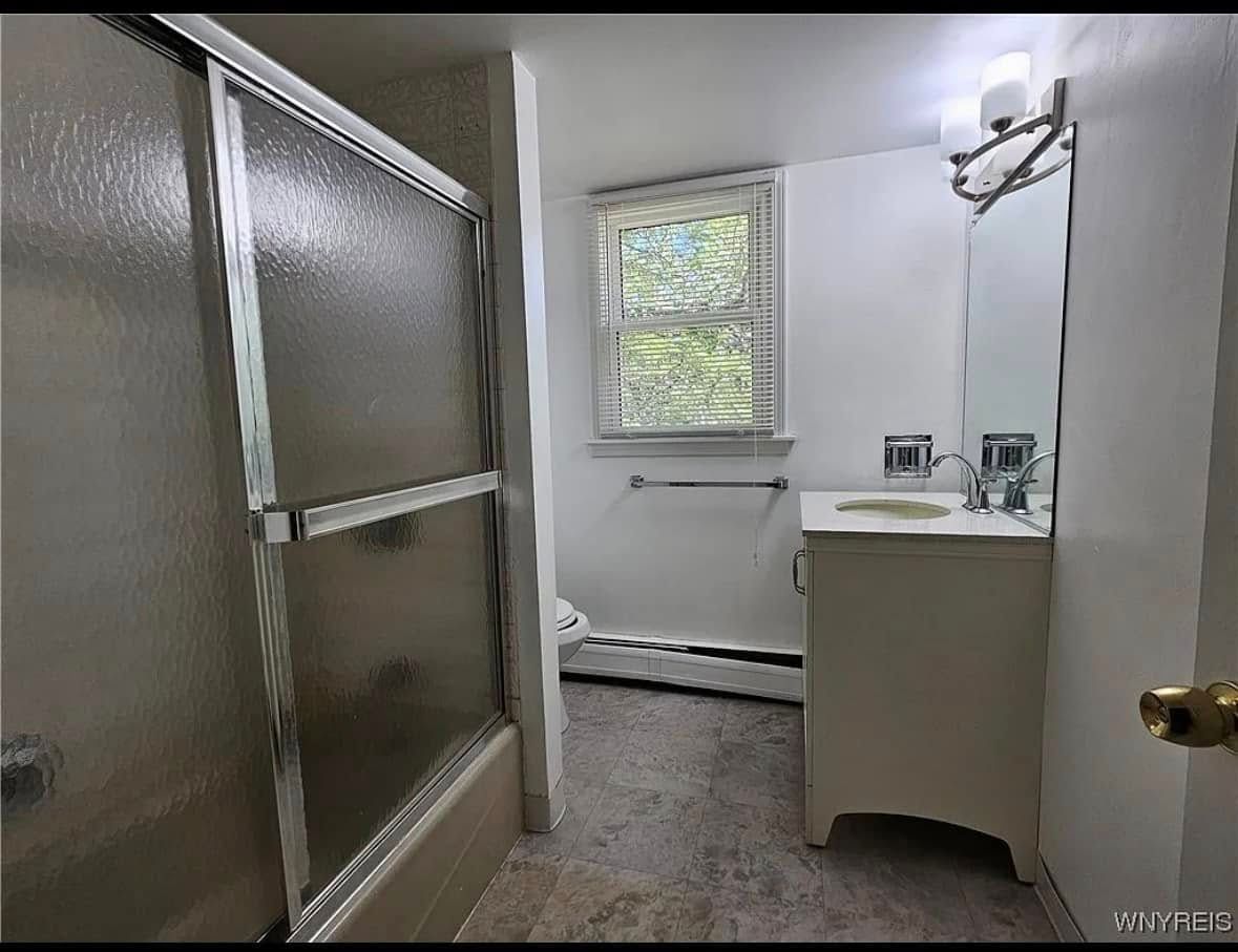 Small bathroom with shower, frosted glass door, window, and white vanity.