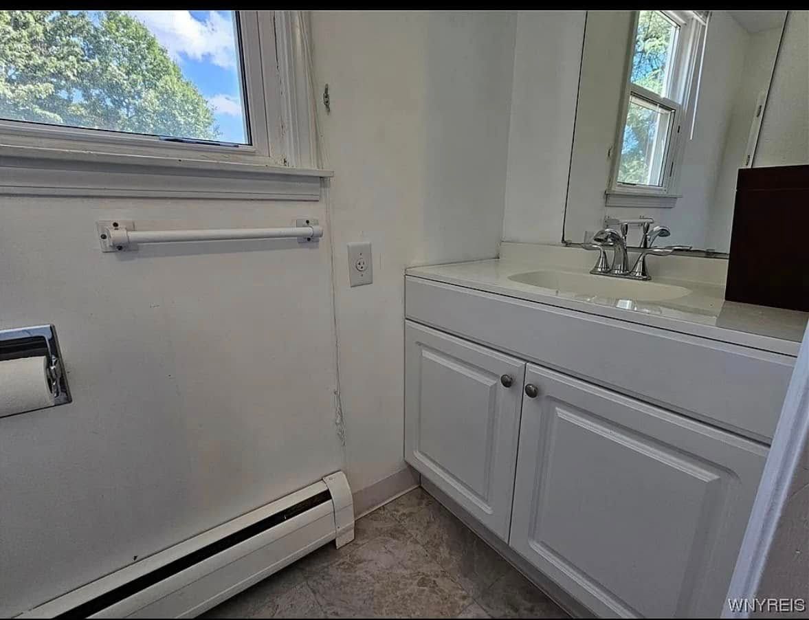 White bathroom vanity with sink beside a window and door, lit by natural daylight.