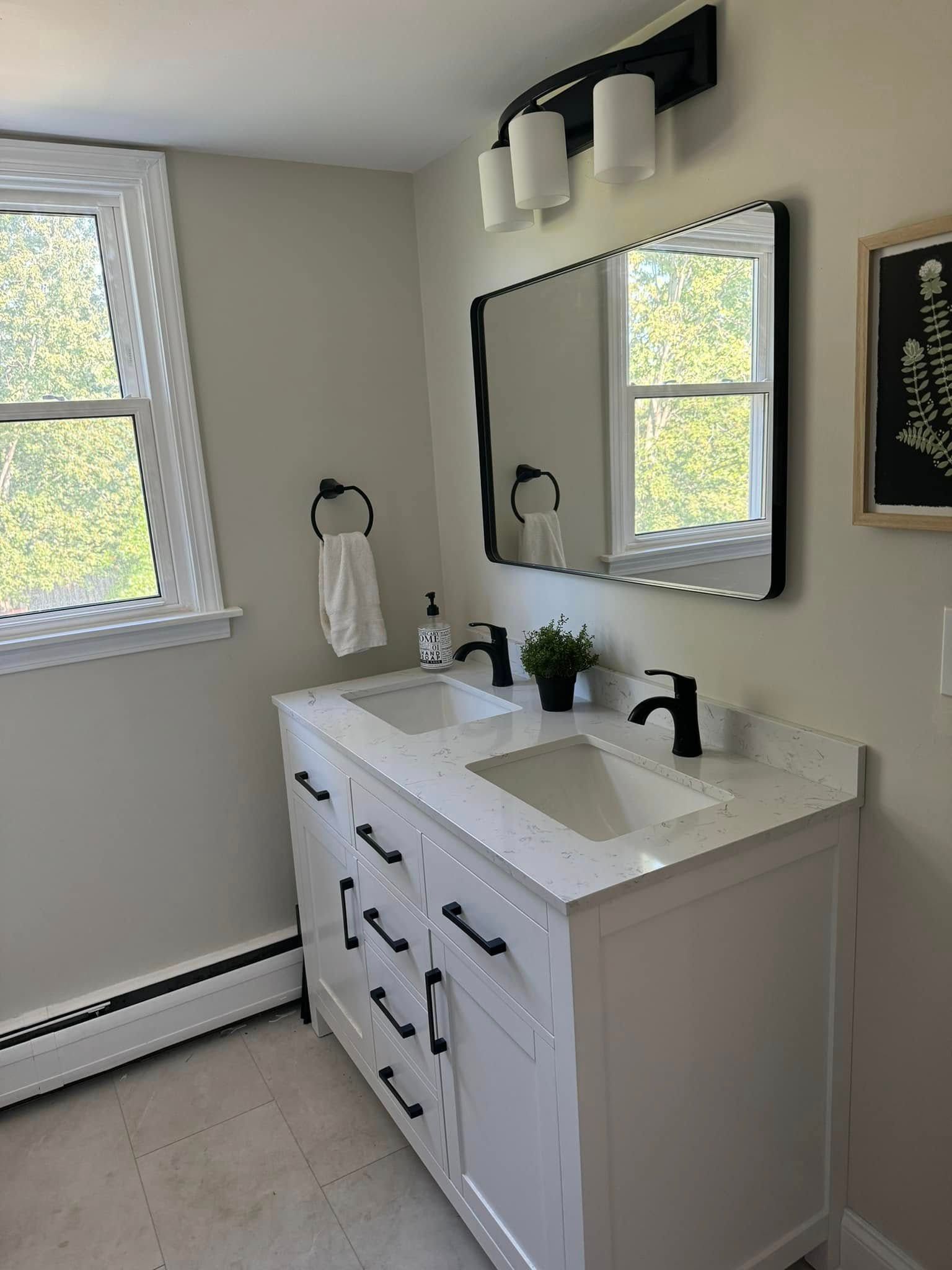 Bright bathroom with white vanity, black fixtures, mirror, and window light.
