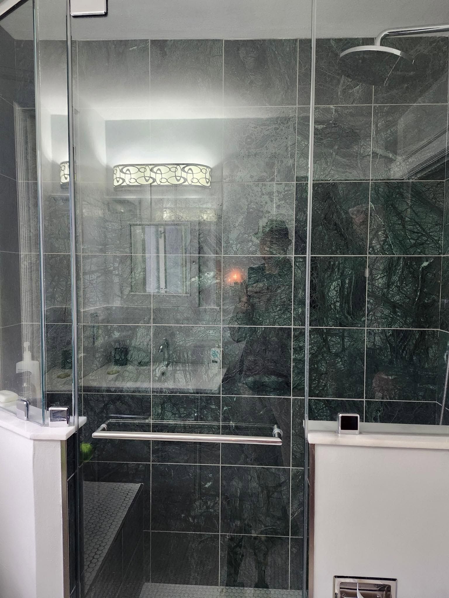 Glass shower enclosure with dark green tile walls and a small window above the doorway
