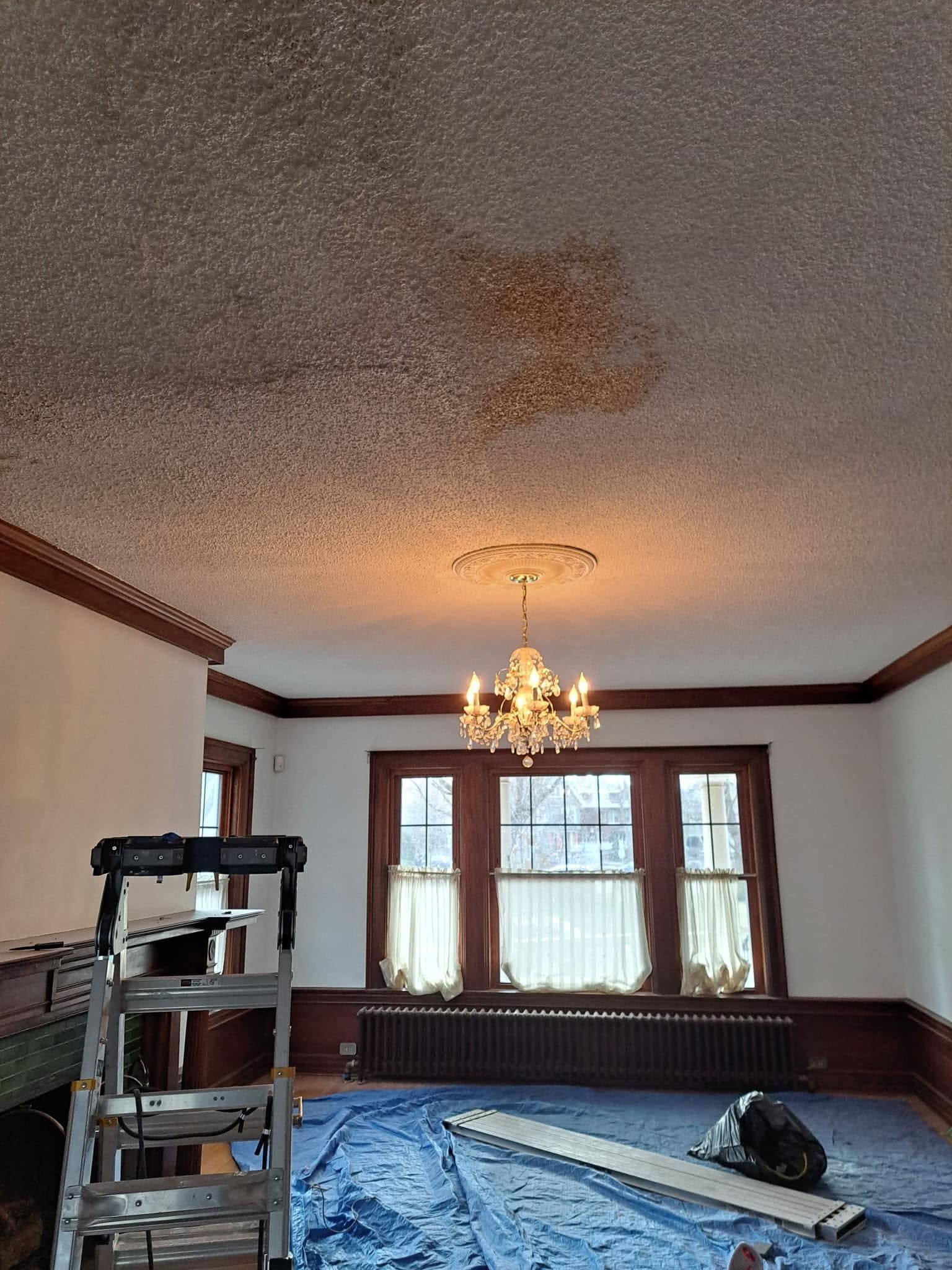Living room with chandelier, tall windows, blue tarp-covered floor, and ladder during renovation