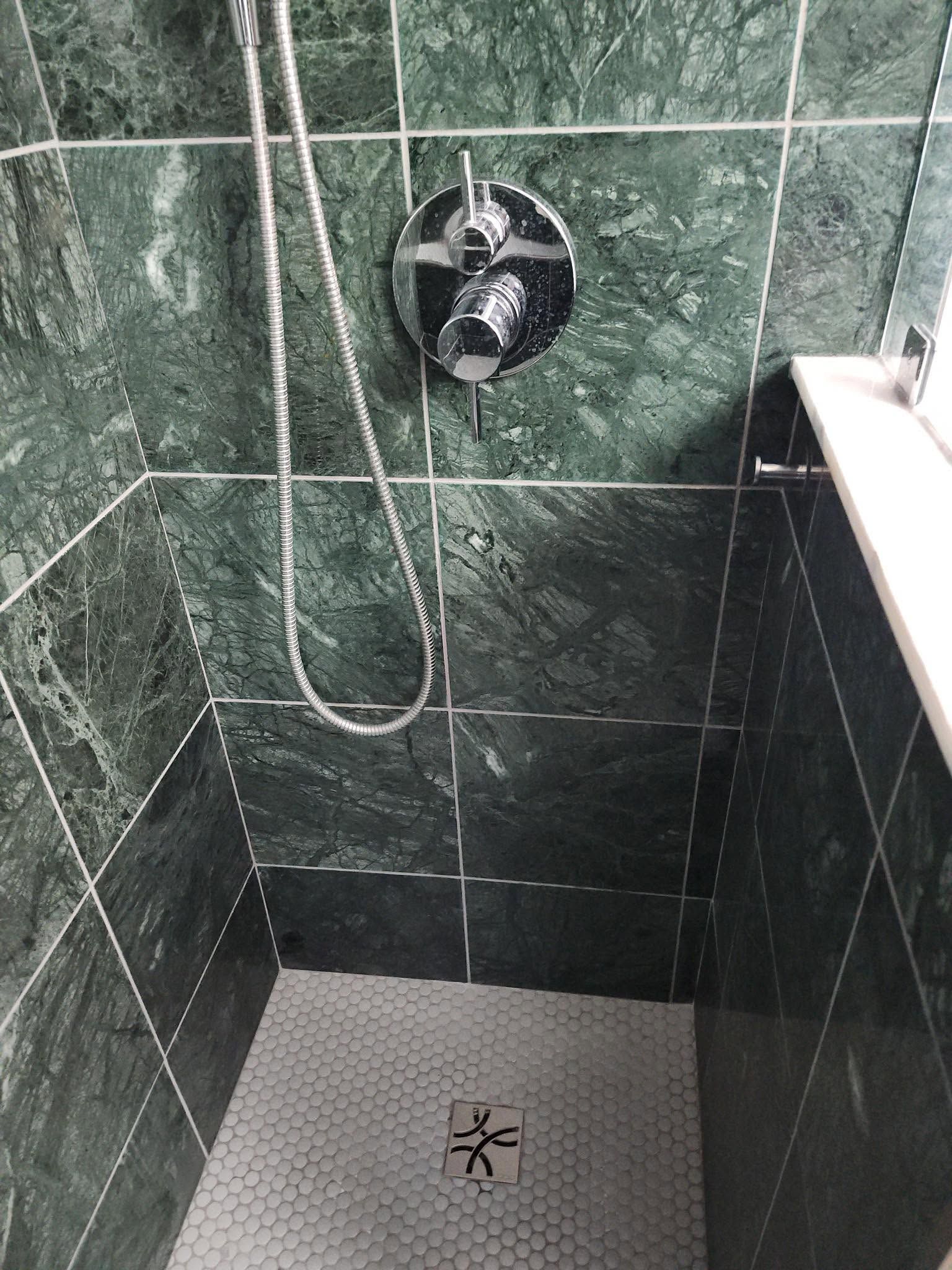 Small shower stall with dark green tile walls, white shower floor, and a chrome shower fixture.