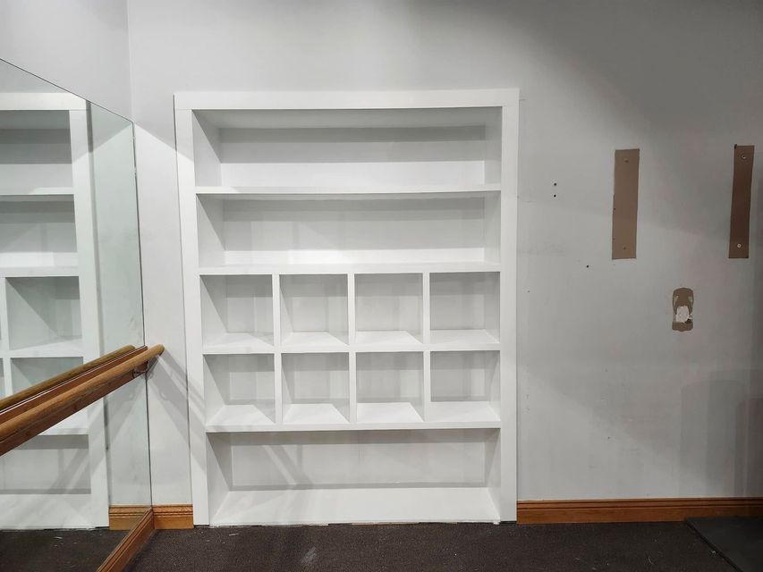 Empty white built-in shelves in a room with a mirror and wooden railing.