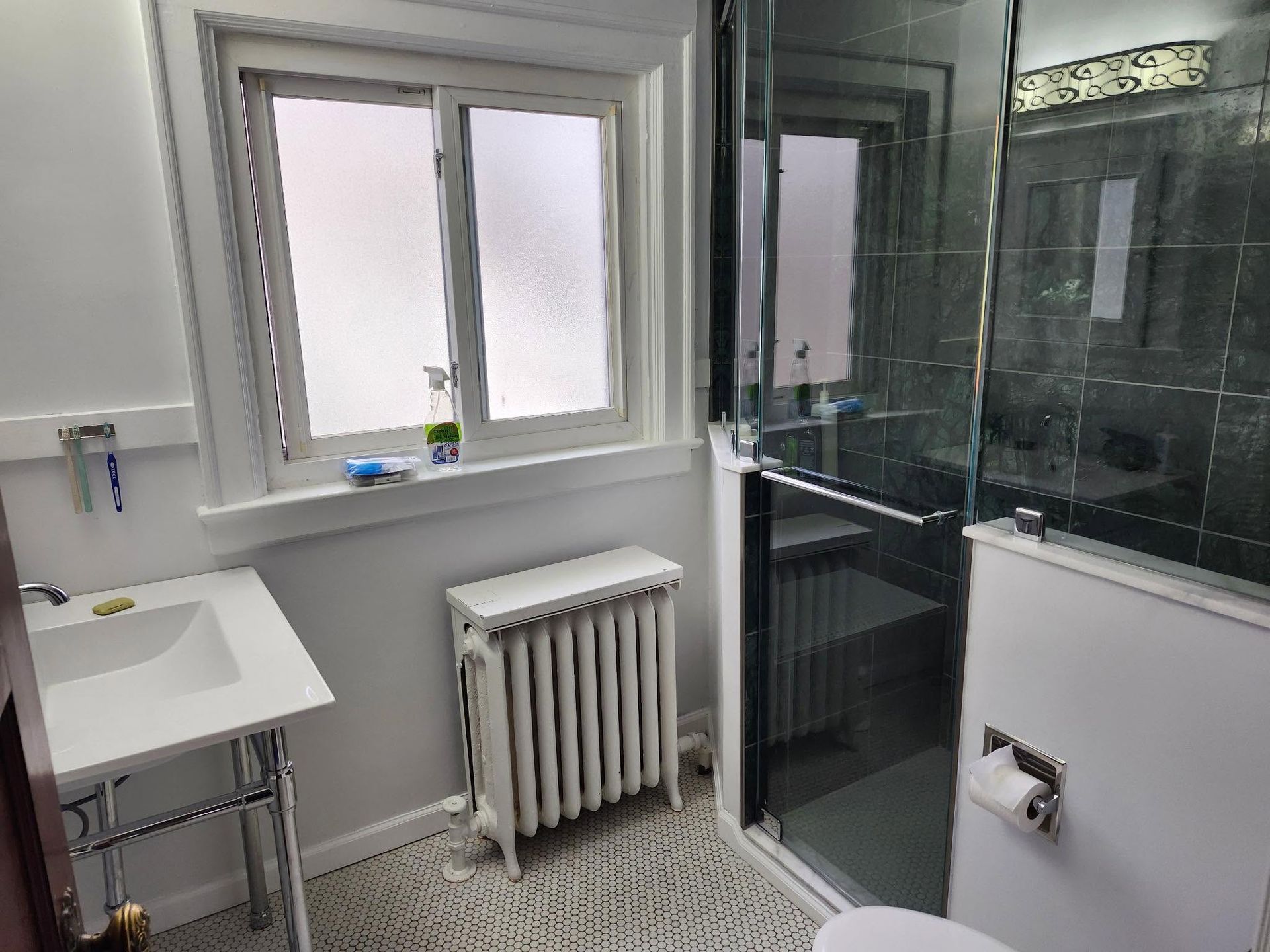 Small white bathroom with sink, radiator, window, and glass shower enclosure
