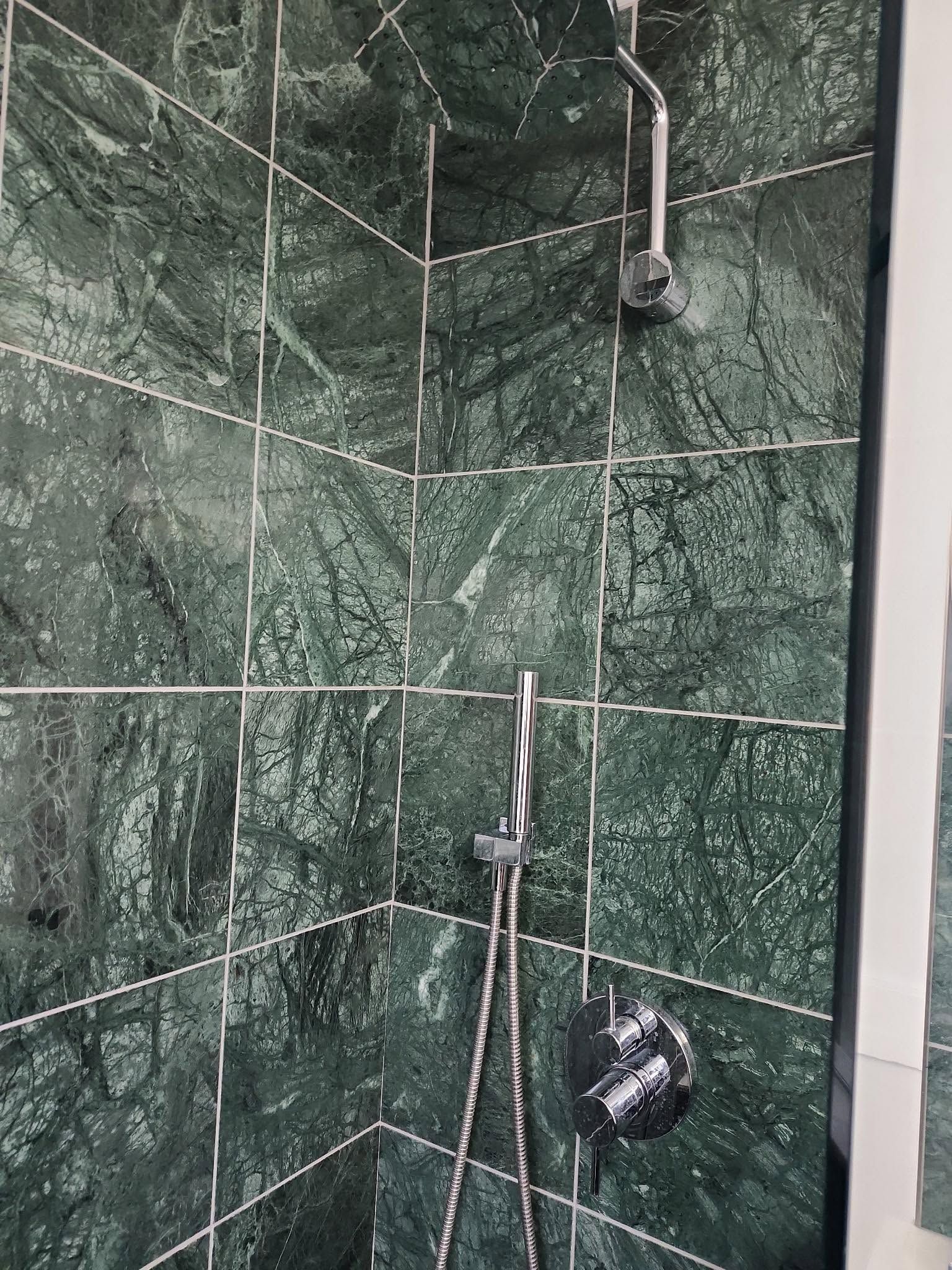Green tiled shower corner with two showerheads and chrome fixtures