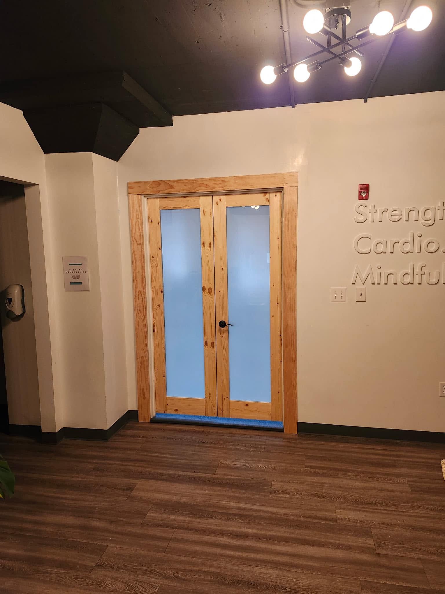 Empty room with wood floors, white walls, and frosted double doors under ceiling lights