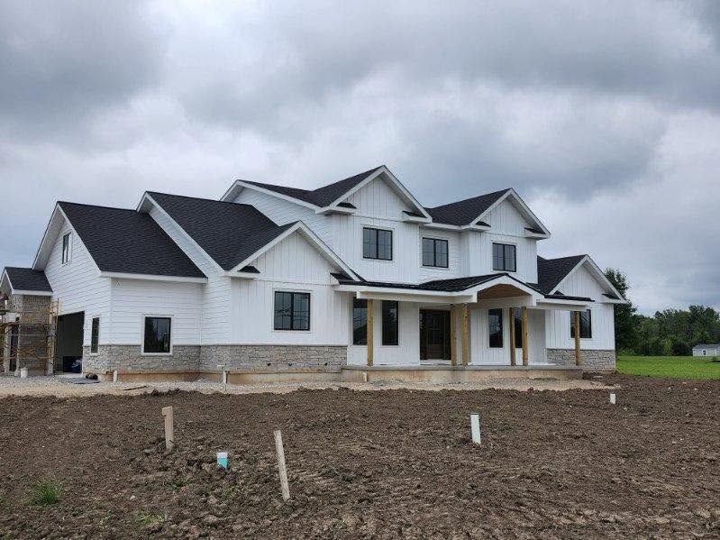 Large white house under construction with dark roofs and a muddy foreground beneath cloudy skies