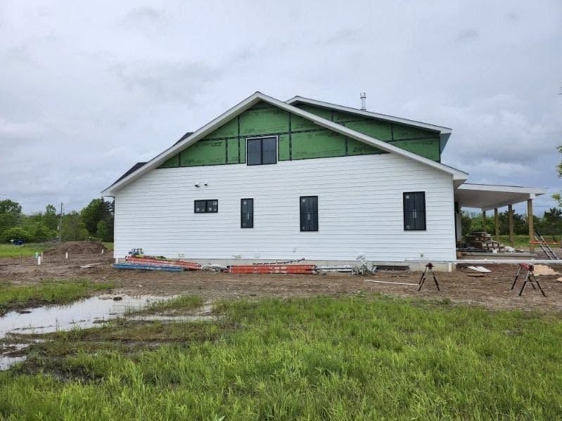 White house under construction with green roof trim, muddy yard, and cloudy sky