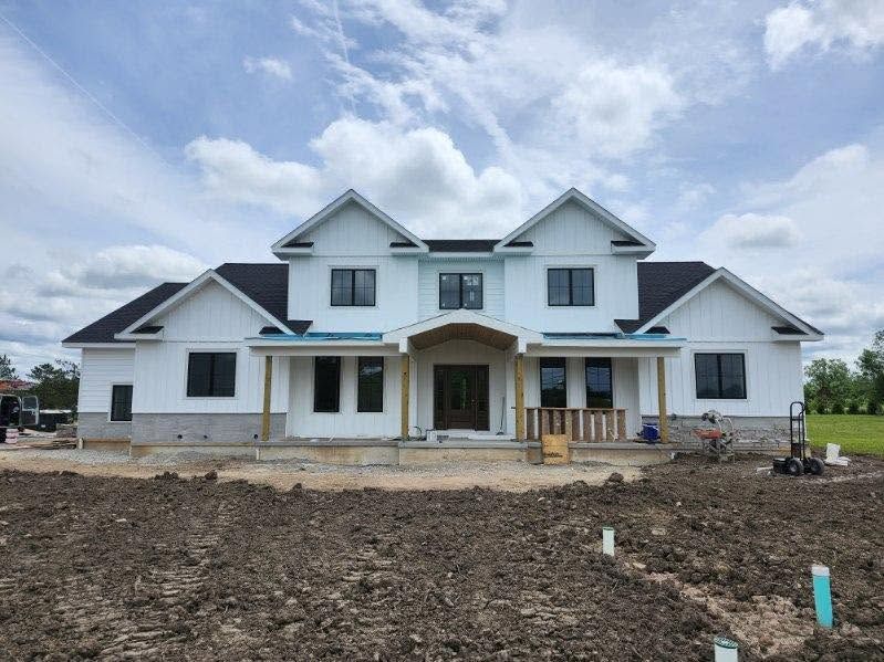 Large white two-story house under construction with a cloudy sky and dirt foreground