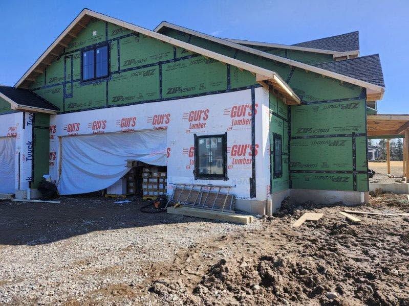 Partially built house with green sheathing and white wrap, surrounded by dirt construction site