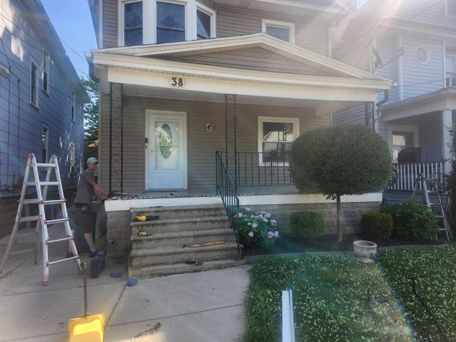 Front porch of a house with steps, a ladder, and a person working near the left side.