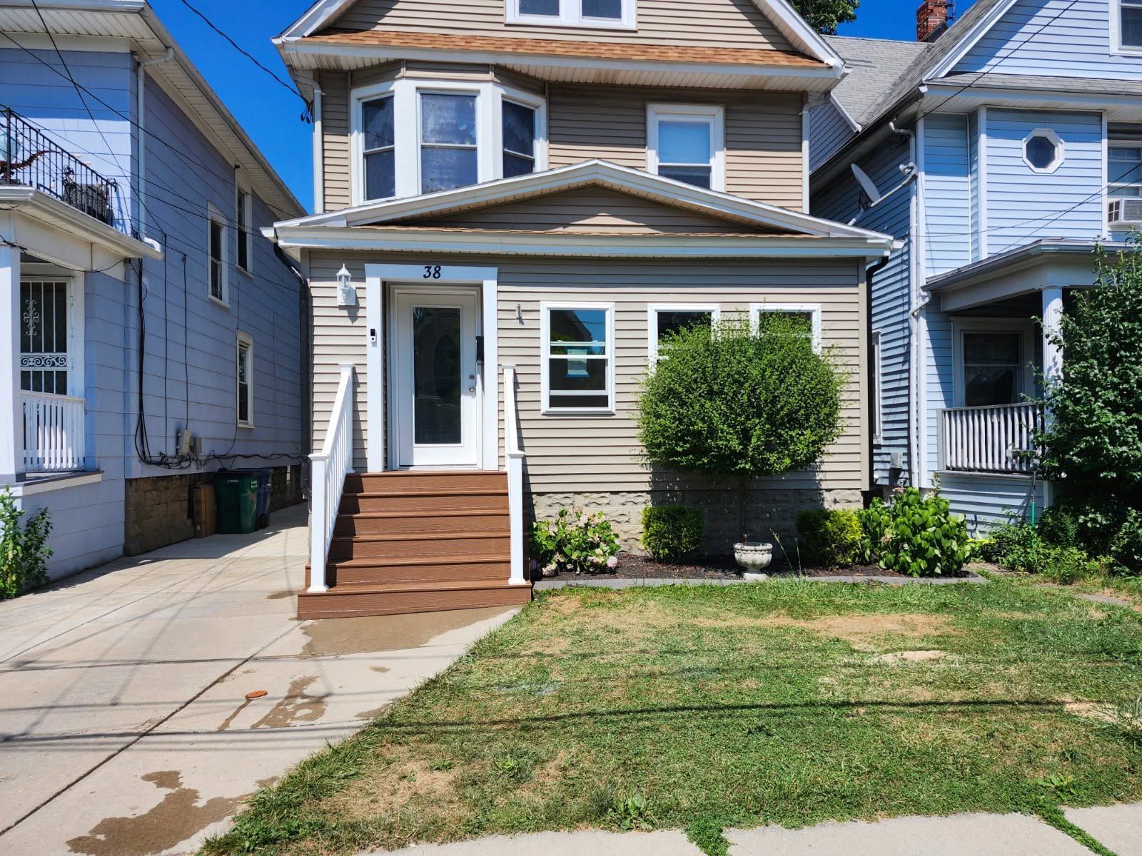 Small beige house with front porch, brown steps, and a patchy front lawn between neighboring homes.