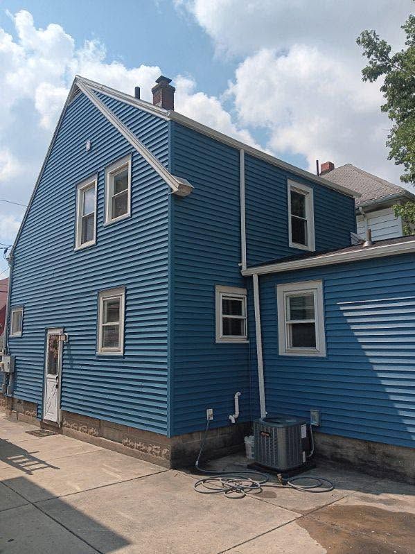 Blue two-story house with white trim, seen from the side on a sidewalk under a partly cloudy sky