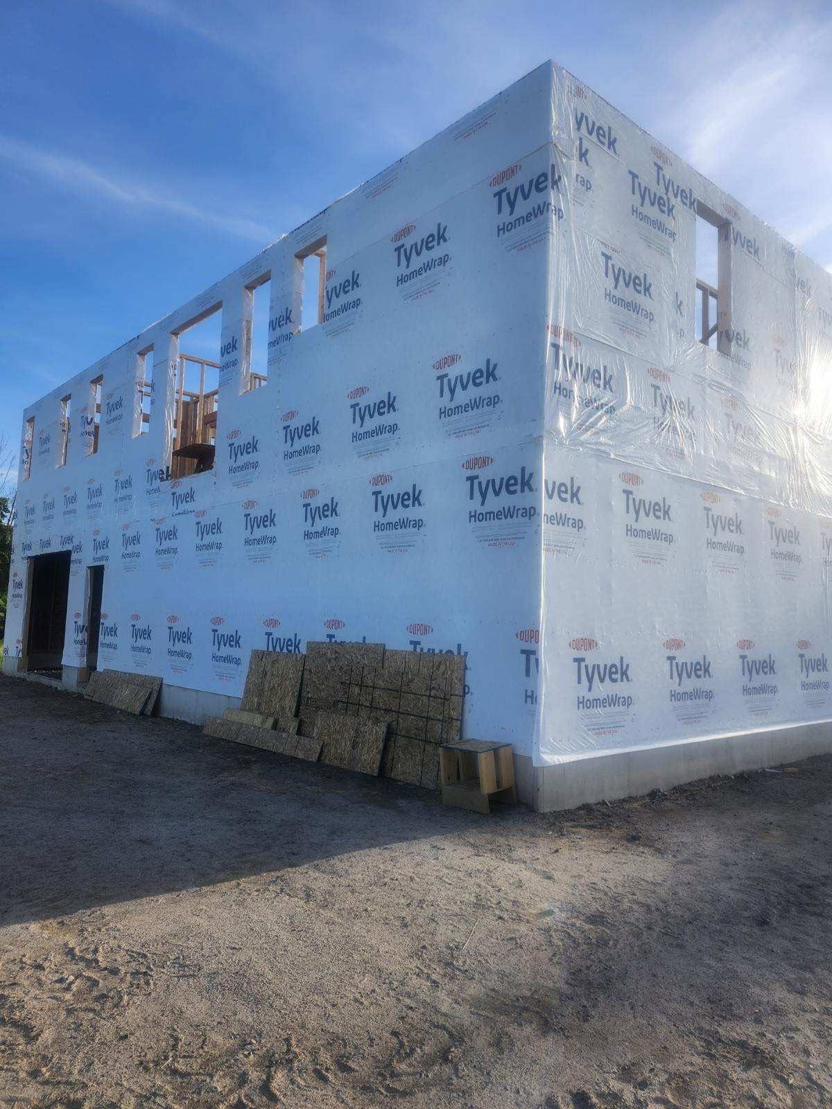 Partially wrapped building under construction with blue Tyvek sheathing and stacked materials outside