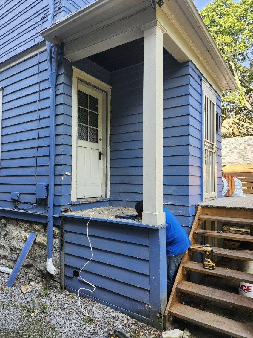Blue house porch with white door and stairs, with a person crouched near the porch railing