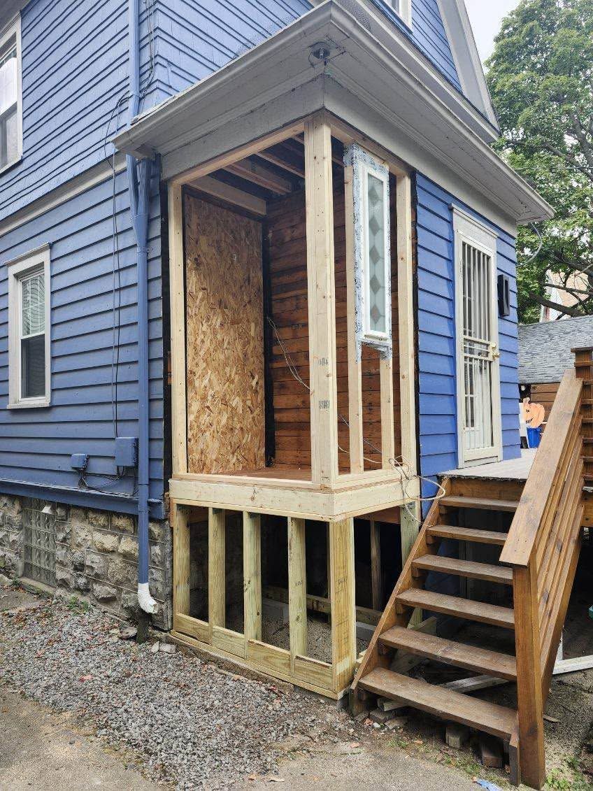 Blue house exterior with a small boarded-in porch and wooden stairs leading to a side door