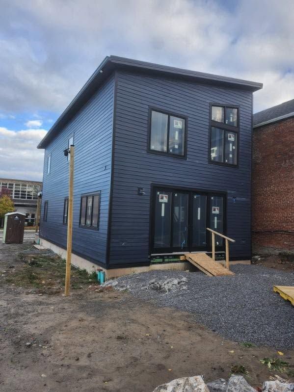 Blue two-story house with dark trim, front steps, and an unfinished gravel driveway